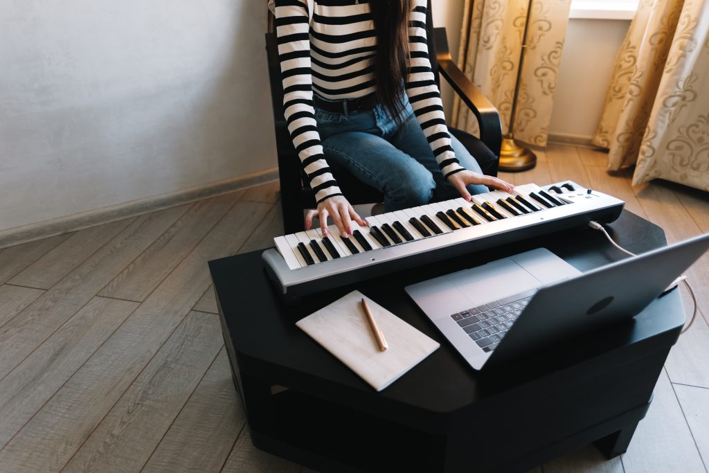 Young caucasian woman learns to play the piano keys using a laptop at home distantly.